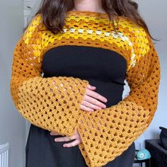 a woman is wearing a yellow and black sweater with crocheted sleeves on her arms