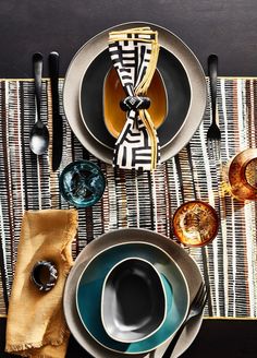 a place setting with plates, cups and spoons on a striped place mat next to utensils