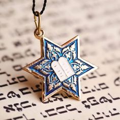 a blue and white star of david necklace on top of an open page of hebrew text