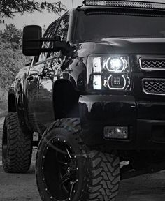 the front end of a black truck parked on top of a dirt road next to trees