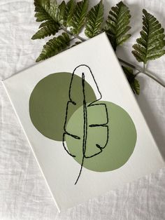 a card with a drawing of a leaf on it next to some green plant leaves