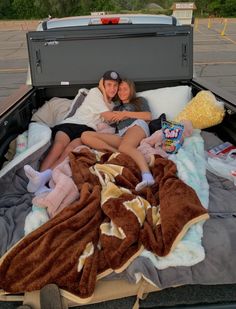 two people are laying in the back of a truck with blankets and stuffed animals on it