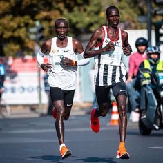 two men running in a race on the street with other people watching from behind them