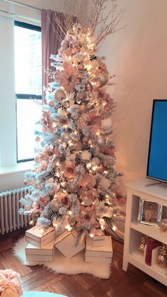 a white christmas tree decorated with pink and silver ornaments in front of a flat screen tv