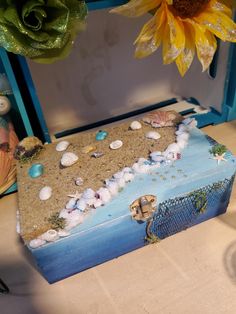 a decorative box with shells and seashells on the bottom sits next to a sunflower