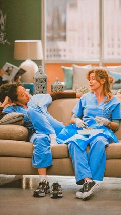 two women in scrubs are sitting on a couch and one woman is laying down