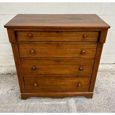 an old wooden chest of drawers sitting on the concrete floor in front of a white brick wall