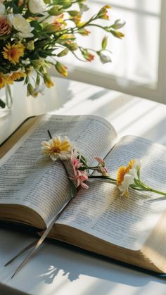 an open book sitting on top of a table next to flowers