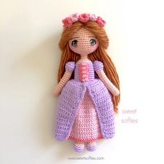 a crocheted doll hanging on the wall with a pink dress and flower in her hair