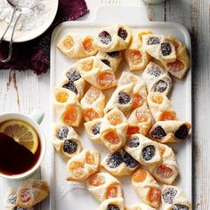 small pastries on a white tray next to a cup of tea and orange slices