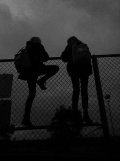 two people with backpacks are standing on a fence