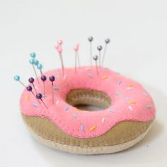 a pink donut with sprinkles and pins sitting on a white surface