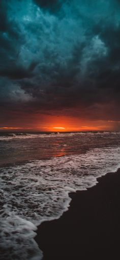 the sun is setting over the ocean with dark clouds in the sky and waves on the beach