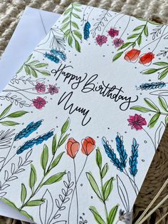 a happy birthday card with flowers and leaves on the front, sitting on top of a wicker basket