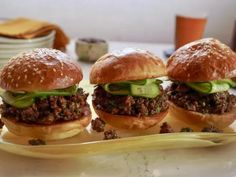 three hamburgers with lettuce and pickles sitting on a plate next to a bowl