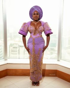 a woman in a purple and gold dress standing next to a window with her hands on her hips