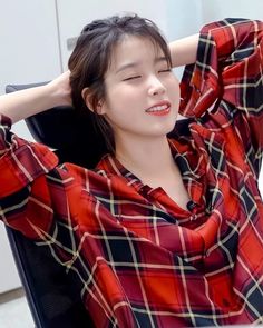 a woman sitting in a chair with her hand on her head and wearing a red plaid shirt