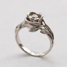 a rose shaped ring with a diamond in the center on a plain surface, ready to be worn