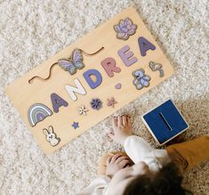 a young child laying on the floor next to a wooden name board with letters and animals