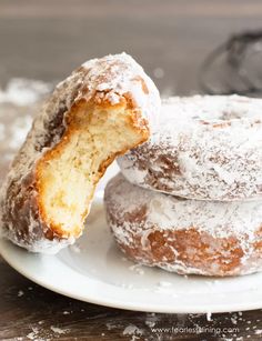 three powdered sugar donuts on a white plate with one bite taken from it