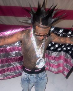 a man with tattoos and piercings standing in front of an american flag