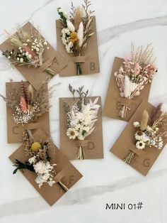 six small cards with dried flowers and feathers on them are laid out on a marble surface