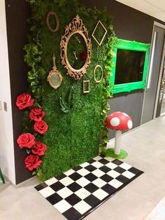 a green wall covered in moss and red flowers next to a black and white checkered floor