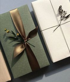 two wrapped gift boxes with ribbons and flowers on the top one is green, white and gold