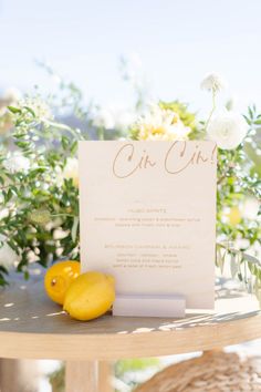 a table with a sign and two lemons on it next to some white flowers