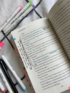 an open book sitting on top of a table next to markers and pens in front of it