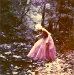 an old photo of a woman in a pink dress walking through the woods with trees