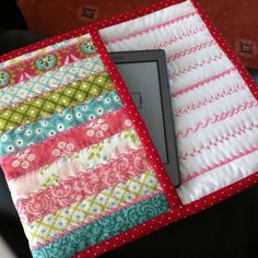 an electronic device sitting on top of a colorful cloth covered tablet case with red polka dot trim