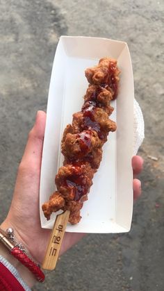 a person holding up a skewer of food on a white plate with red sauce