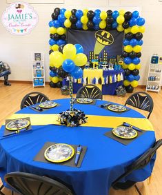 a batman themed birthday party with blue and yellow table cloths, black and white plates, and balloons