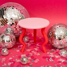 a small table surrounded by disco balls and confetti on a pink background,