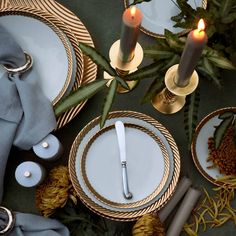 the table is set with plates, silverware and pine cones