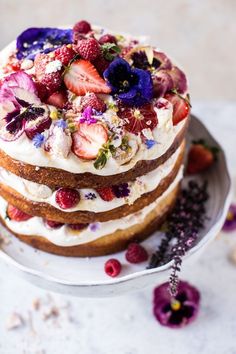 a layered cake with strawberries and blue flowers on top is sitting on a plate