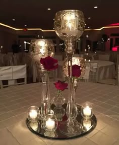 the centerpiece is made out of glass and has candles, roses, and votives on it