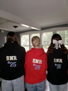 three girls in black and red sweatshirts looking out the window with white bows on their hair