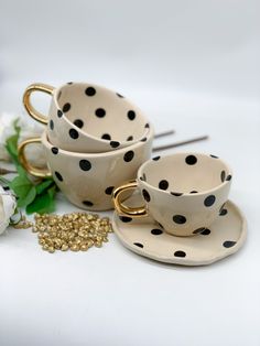 polka dot tea cups and saucers with gold rims on white surface next to flowers