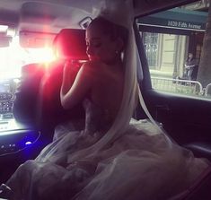 a woman sitting in the back seat of a car wearing a wedding dress and veil