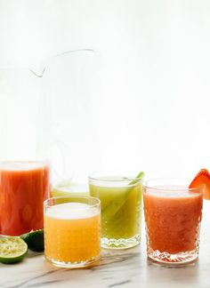 three glasses filled with different types of drinks on a table next to fruit and watermelon