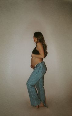 a pregnant woman in jeans is posing for the camera while holding her belly up and looking down