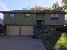 a two story house with green siding on the front and side of it, surrounded by grass