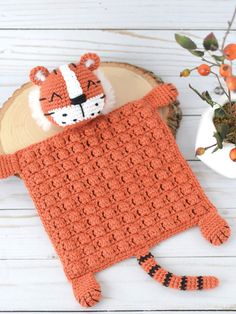 a crocheted tiger sleeping bag next to a potted plant on a white wooden table