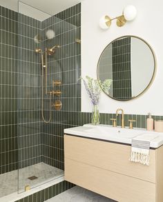 a green tiled bathroom with gold fixtures and a round mirror on the wall above the sink