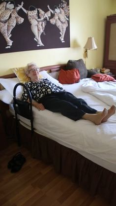 an older woman laying on top of a bed in a bedroom next to a painting