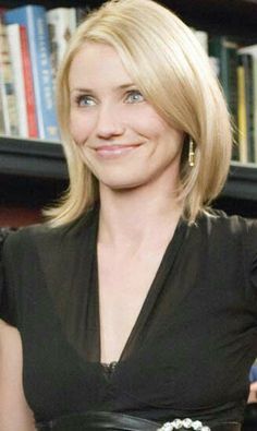 a woman in a black dress is holding a book and smiling at the camera while standing next to a bookshelf