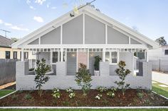 a grey house with white trim and shutters on the front door is surrounded by plants