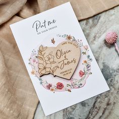 a wooden heart shaped brooch sitting on top of a piece of paper next to a pink flower